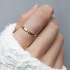 Anillo abierto dorado con iniciales en la mano, sobre un jersey blanco
