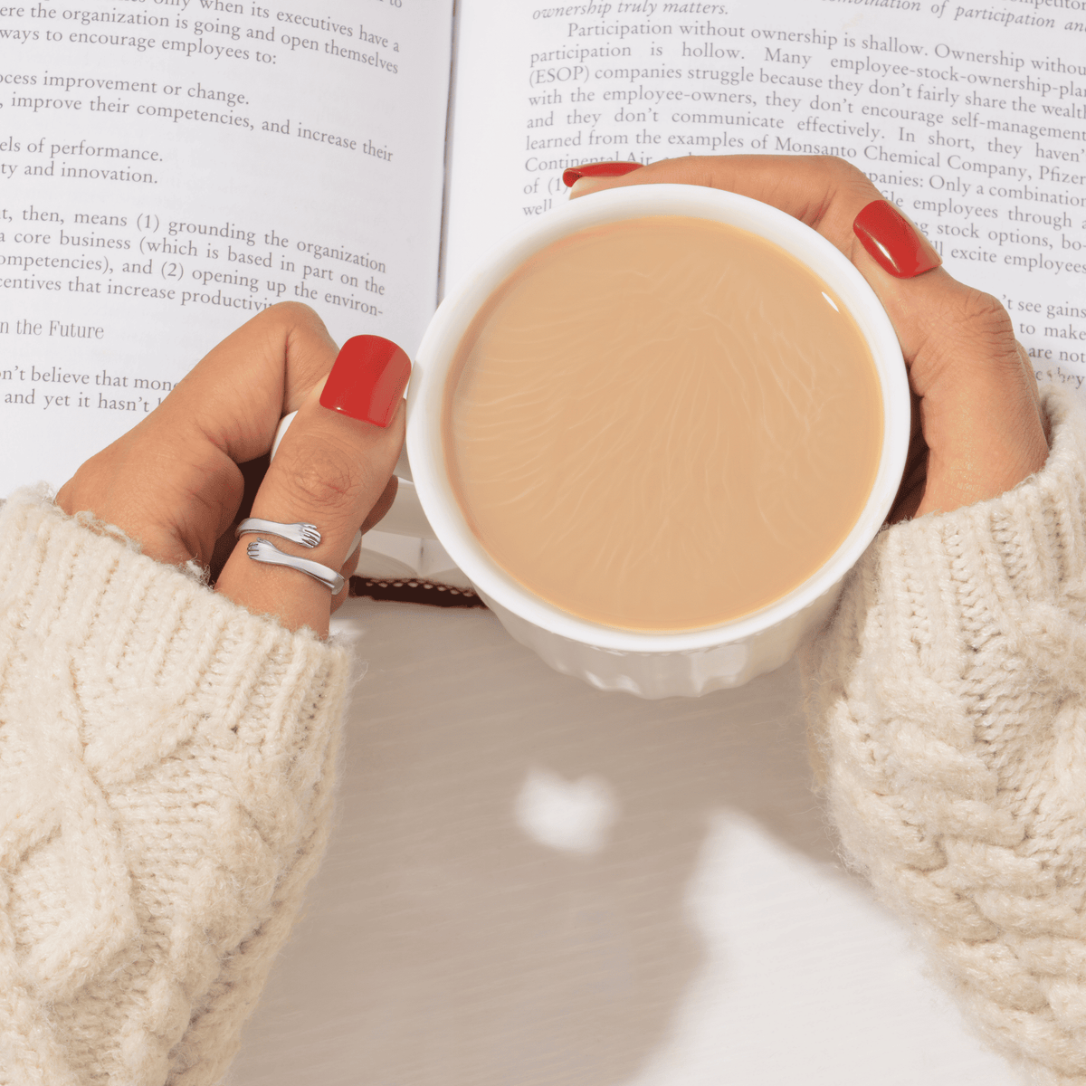 Anillo abrazo puesto en la mano, sujetando una taza de café